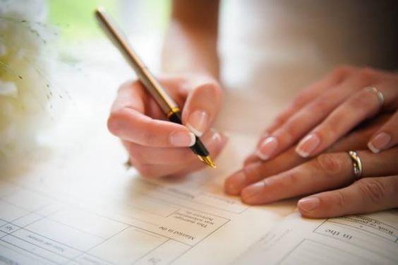 mão com unhas decoradas assinando papéis do casamento civil