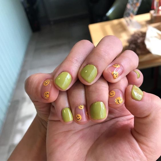 unhas pintadas com esmalte verde com decorações de emojis sorrindo