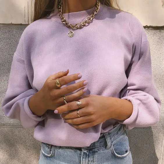 mulher vestindo blusão roxo com mãos decoradas de esmalte roxo