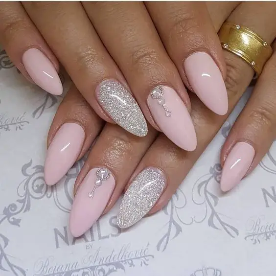 Modelo de unhas amendoadas rosa bebê com glitter e jóias