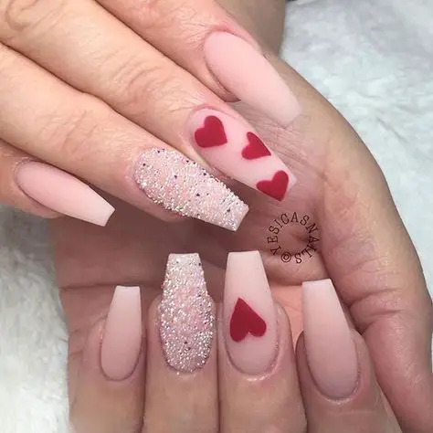 Exemplo de unhas rosa fosca com corações vermelhos e joias