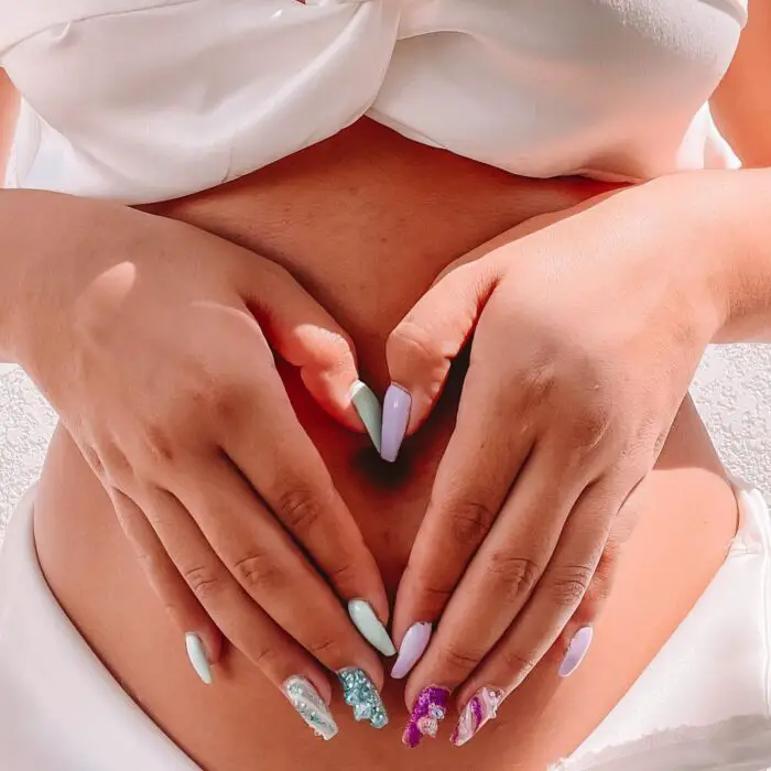 Mão com unhas decoradas na barriga grávida