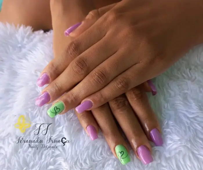 Esmaltação verde e roxa com desenho de coração em uma das unhas