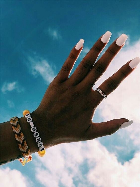 Foto de mão morena com unhas brancas e céu no fundo