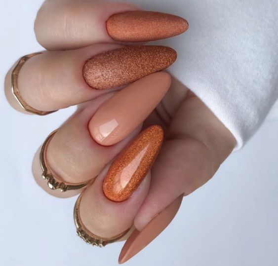 Modelo de nails amendoadas compridas em tons de caramelo com glitter