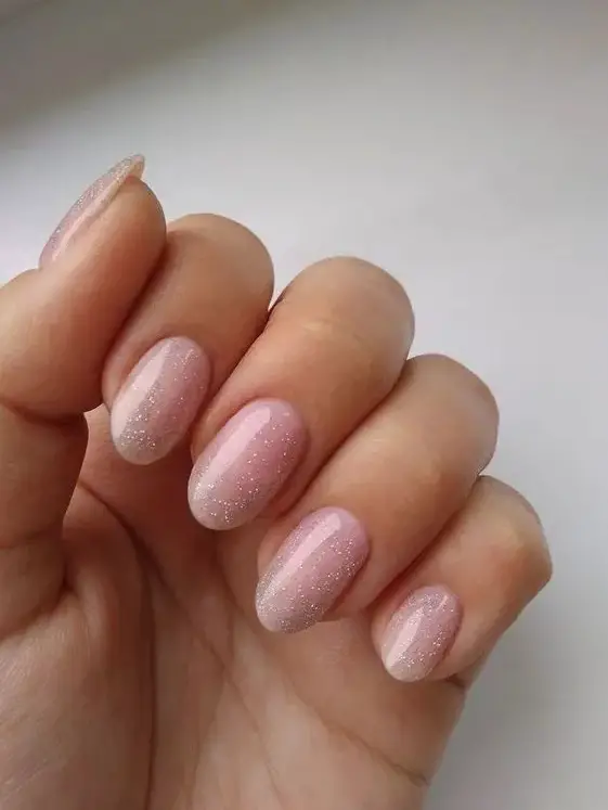 Foto de unhas com esmalte clarinho e uma camada de glitter