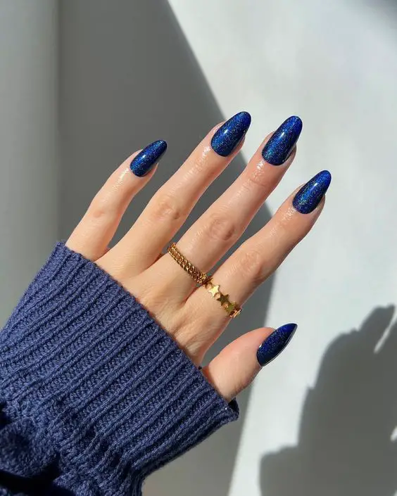 mão feminina exibindo suas unhas decoradas na cor azul escuro com brilhos