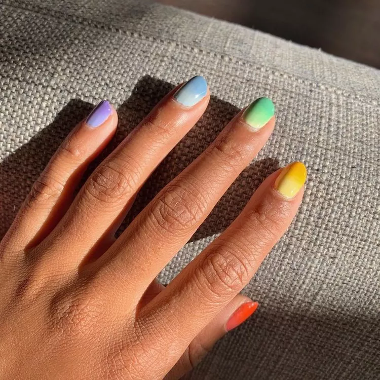 mãos com unhas pintadas com cores em degrade coloridas